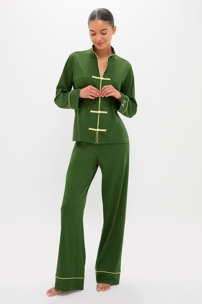 Woman models Douglas Fir Pima Cotton Wilford Women's Pajama Set, featuring a classic mandarin collar, effortless frog-style closures, and high-end yellow piping on forest-green fabric.
