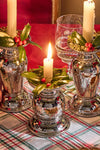 Graham 5 Pillar/Taper Candle Holder: Three classic, hammered metal holders with taper candles, one lit, surrounded by festive holly wreaths on a plaid tablecloth, creating an effortless, high-end holiday ambiance.