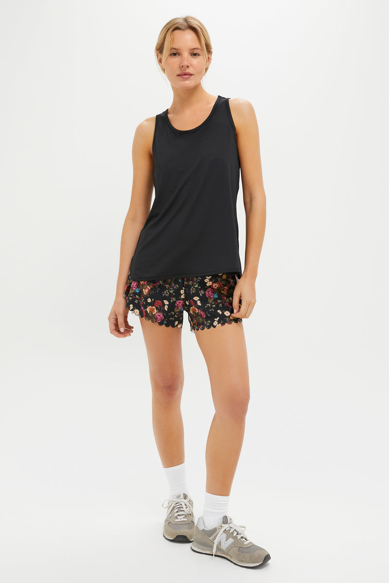A person in a Tnuck Sport black racerback tank, black floral quick-dry shorts, white socks, and gray sneakers stands against a plain white background.