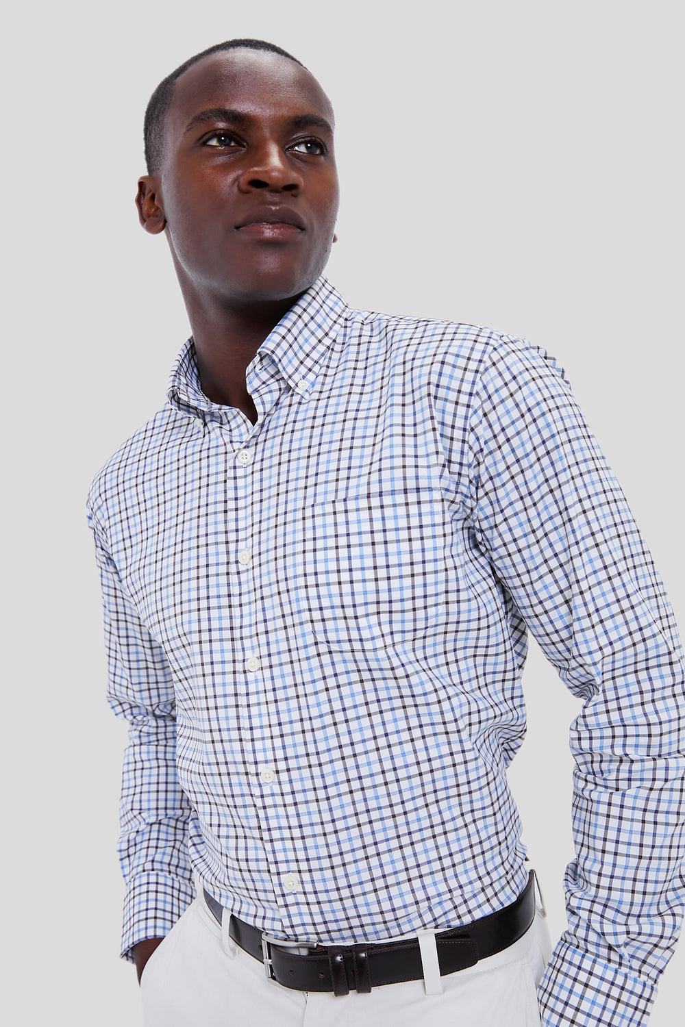Man in a blue and white Peter Millar sport shirt, paired with white pants and a black belt, showcases sophisticated style crafted from advanced performance yarns.