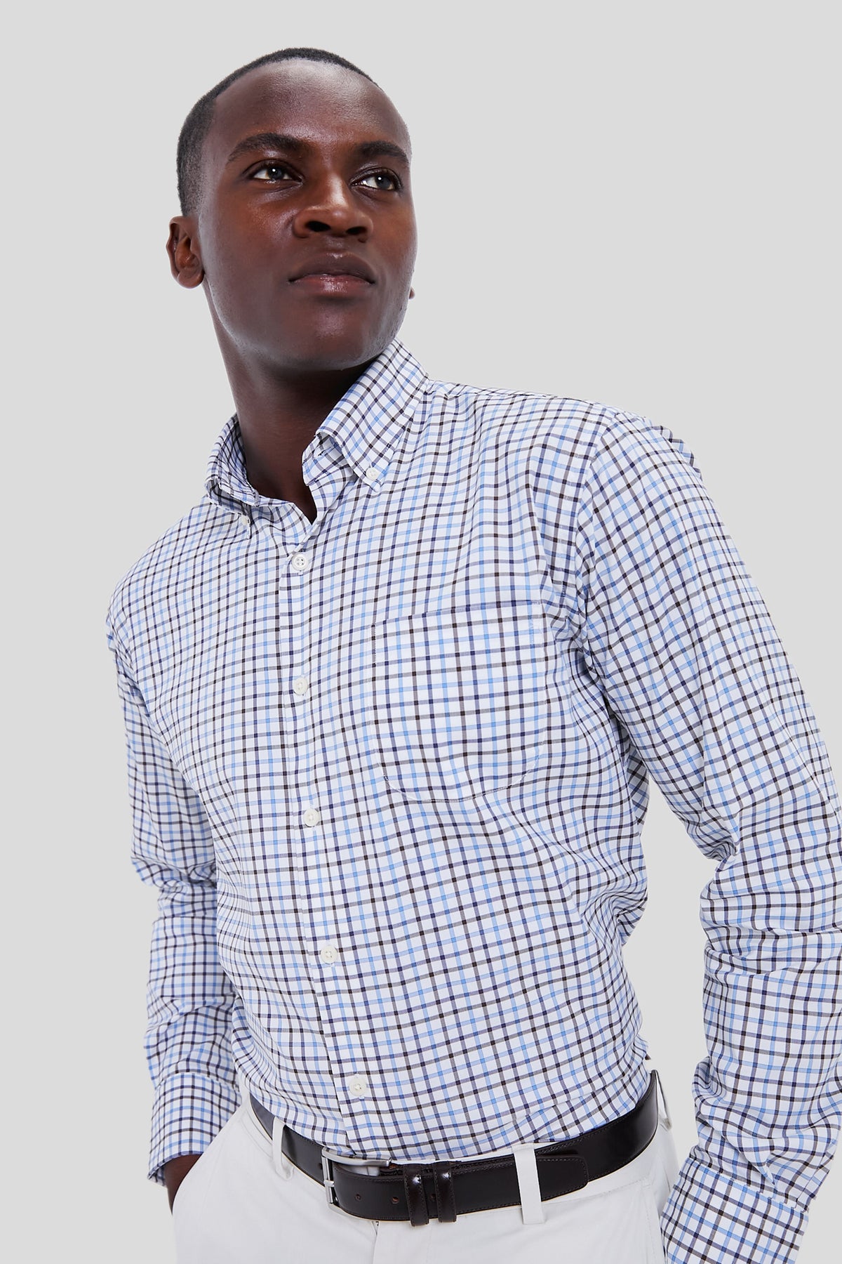 Man in a blue and white Peter Millar sport shirt, paired with white pants and a black belt, showcases sophisticated style crafted from advanced performance yarns.