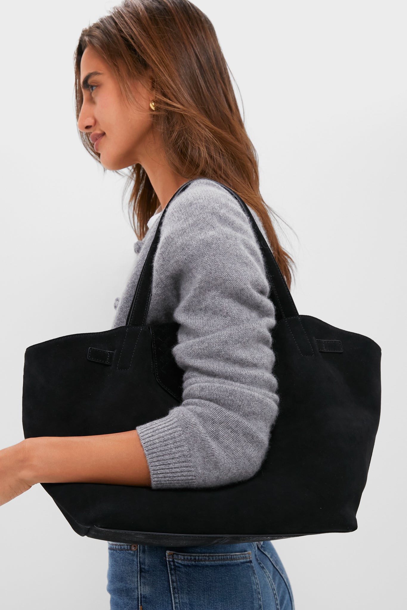 Woman carrying the Black Suede Blaine Tote, a classic, high-end bag with an effortless style, featuring top handles and a woven flap for a fun, polished look.