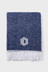 A Matouk folded navy throw features a white fringe hem and the monogram ACB embroidered in white on the front.
