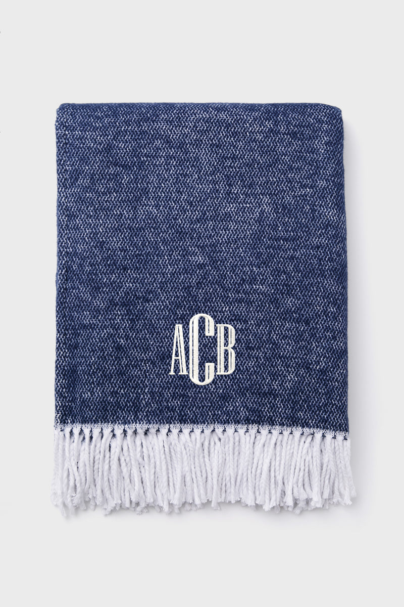 A Matouk folded navy throw features a white fringe hem and the monogram ACB embroidered in white on the front.