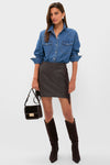 Woman wearing the Coffee Faux Faux Leather Fringe Paddock Mini Skirt, styled effortlessly with a denim shirt and knee-high boots for a classic, high-end, fun look.