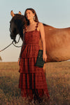 Woman wearing a sleeveless maxi dress with eyelet details in a rust color standing next to a horse. 