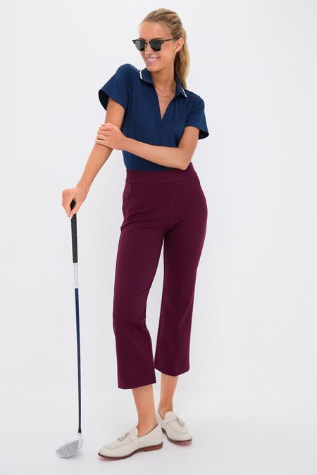 Woman in sporty-casual outfit, showcasing the Petite Winetasting Compression September Pant with a classic, effortless style, holding a golf club against a white backdrop.