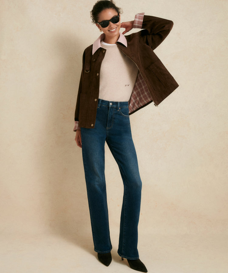 Woman in a brown jacket with a pink collar, a tan sweater, and jeans. 