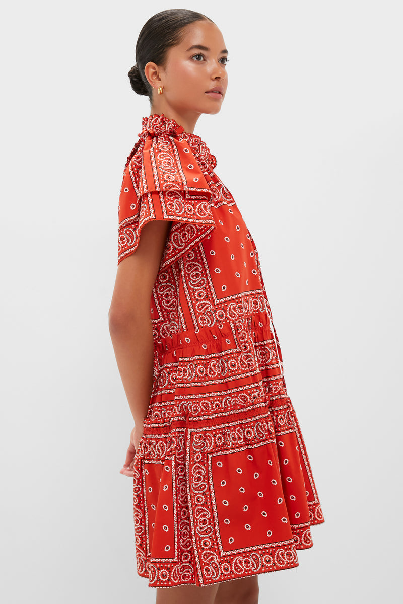 A woman stands against a white background, wearing a Hunter Bell red bandana-print swing mini dress with ruffled high neckline and short sleeves, crafted from 100% cotton.