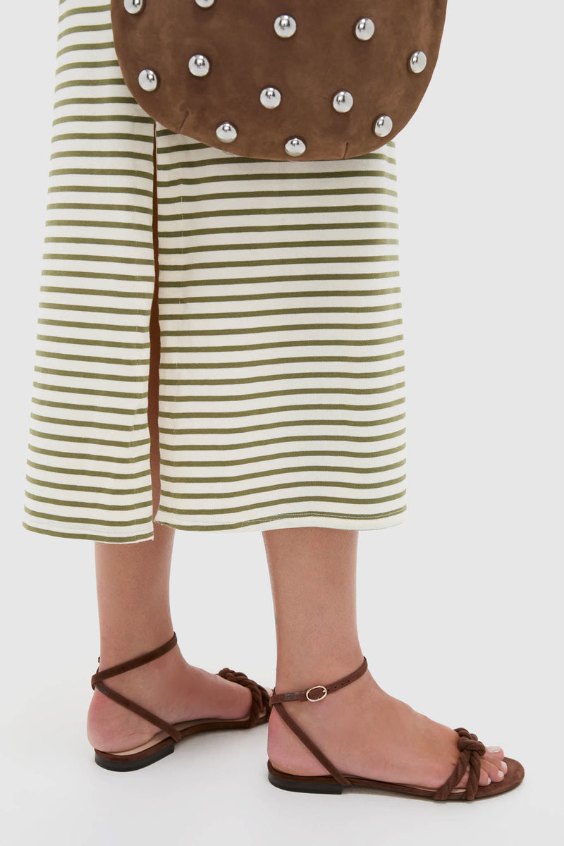 A person wearing a Pomander Place olive stripe maxi dress with brown flat sandals, carrying a brown bag decorated with silver studs.