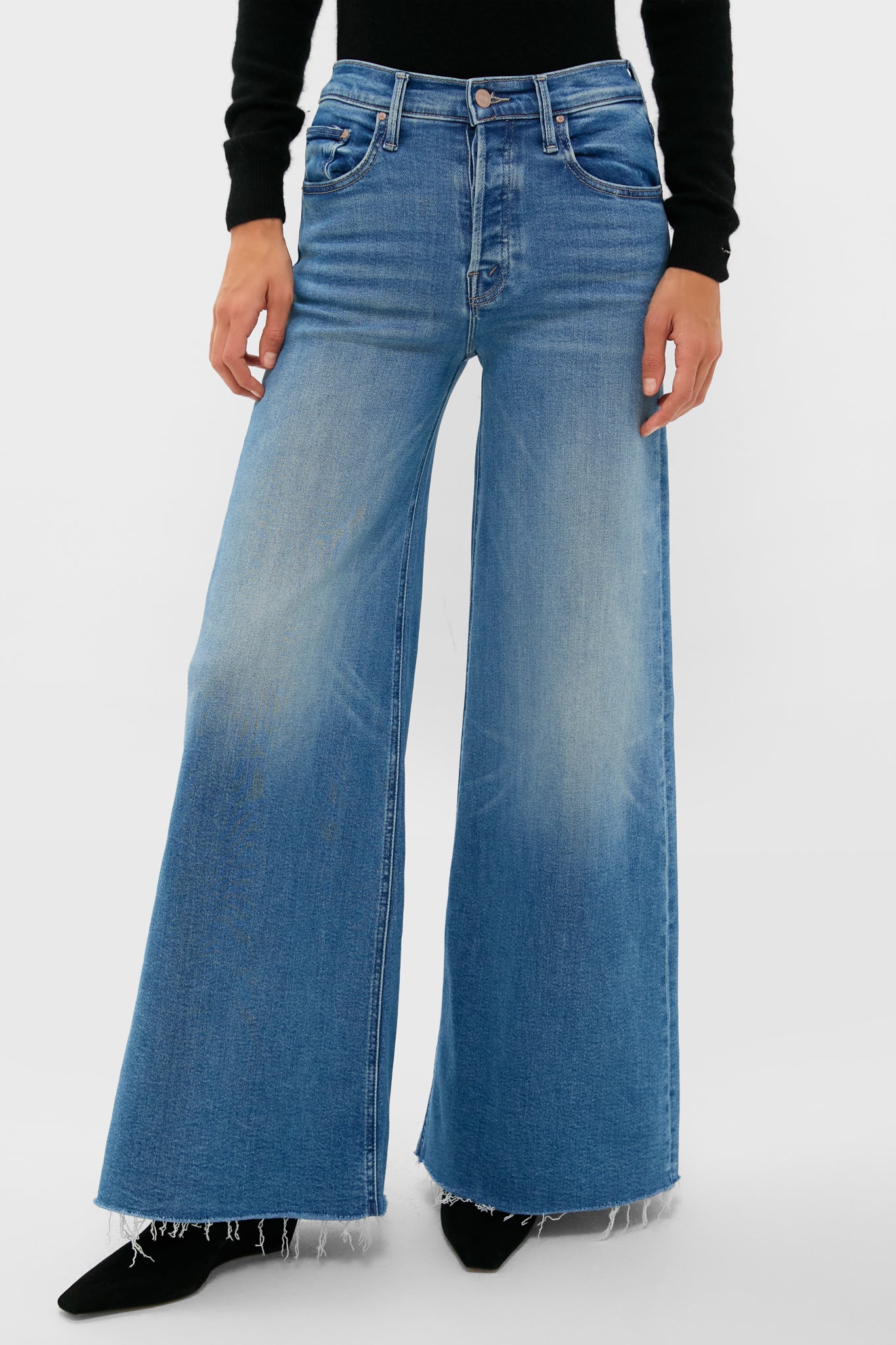 A person wearing MOTHER high-waisted wide-leg stretch denim jeans with a frayed hem and a black long-sleeve top, standing confidently.