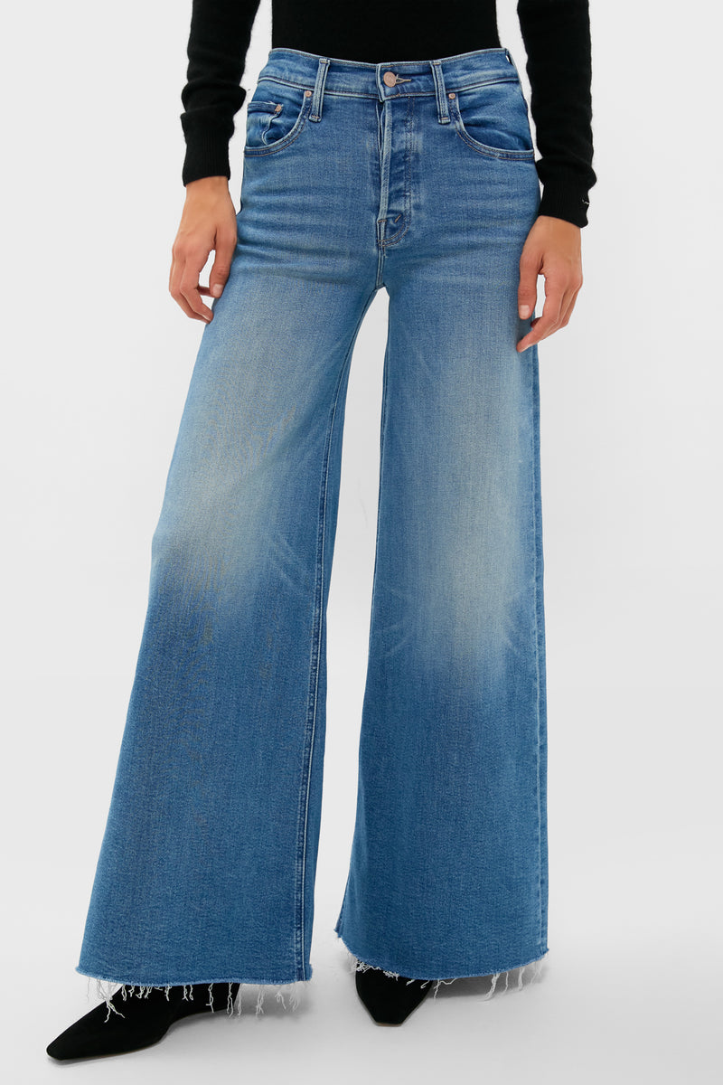 A person wearing MOTHER high-waisted wide-leg stretch denim jeans with a frayed hem and a black long-sleeve top, standing confidently.