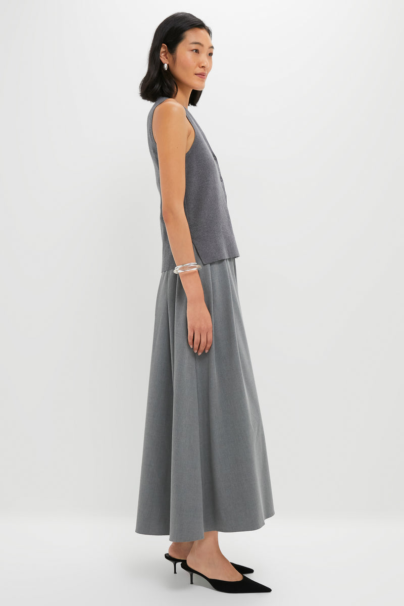 A woman in profile wears the STAUD Madeline Dress—a sleeveless grey cotton cashmere transitional piece—styled with black slingback heels and silver bracelets against a plain white background.