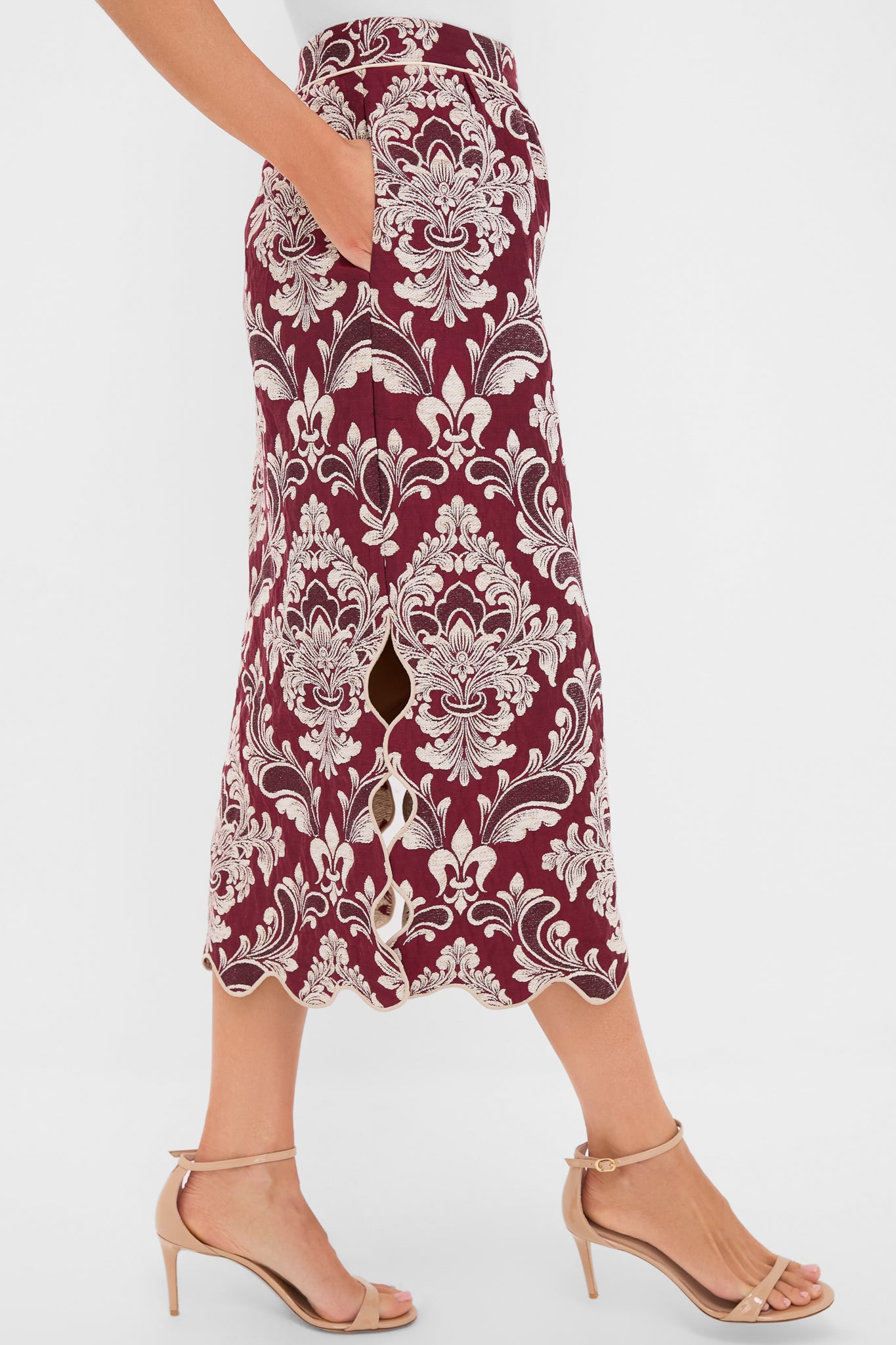 Woman modeling the Blush Pink and Burgundy Bicolor Jacquard Waves Midi Skirt with a scalloped hem and side pockets, paired with beige strappy stilettos for an effortless, high-end look.