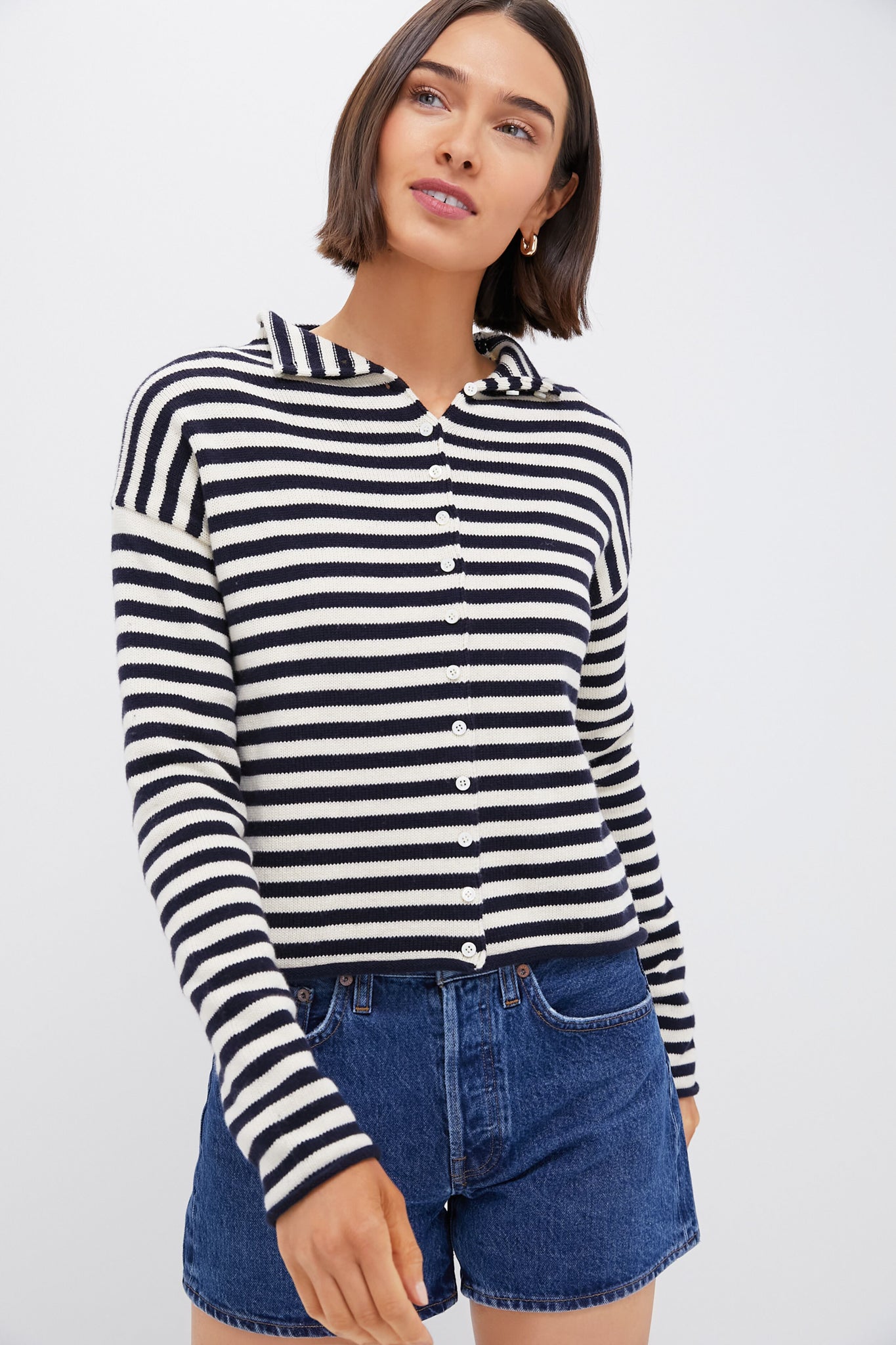 Woman in an Alex Mill Navy Ivory Taylor Cardigan with black and white stripes and a collar, styled with blue denim shorts—a look that showcases classic essentials and timeless style.