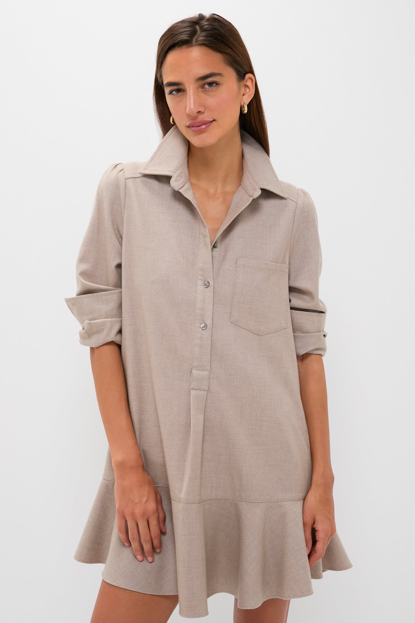 A woman models the Tuckernuck Callahan Shirt Dress in light beige, featuring long sleeves, a chest pocket, a ruffled hem, and a relaxed fit against a plain white background.