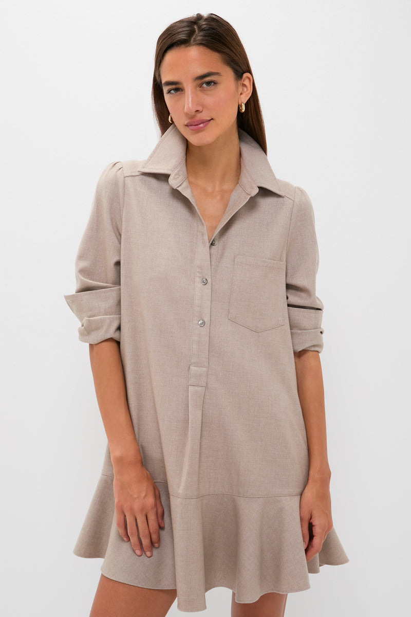 A woman models the Tuckernuck Callahan Shirt Dress in light beige, featuring long sleeves, a chest pocket, a ruffled hem, and a relaxed fit against a plain white background.