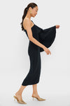Model wearing Black Bidi Bidi Bom Bom Tea Length Dress; features an asymmetrical neckline and dramatic ruffled sleeve, paired with gold accessories for a classic, high-end, and effortless look.