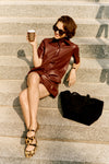 Woman sitting on stairs with a cup of coffee in a brown leather mini dress and cheetah ballet flats. 