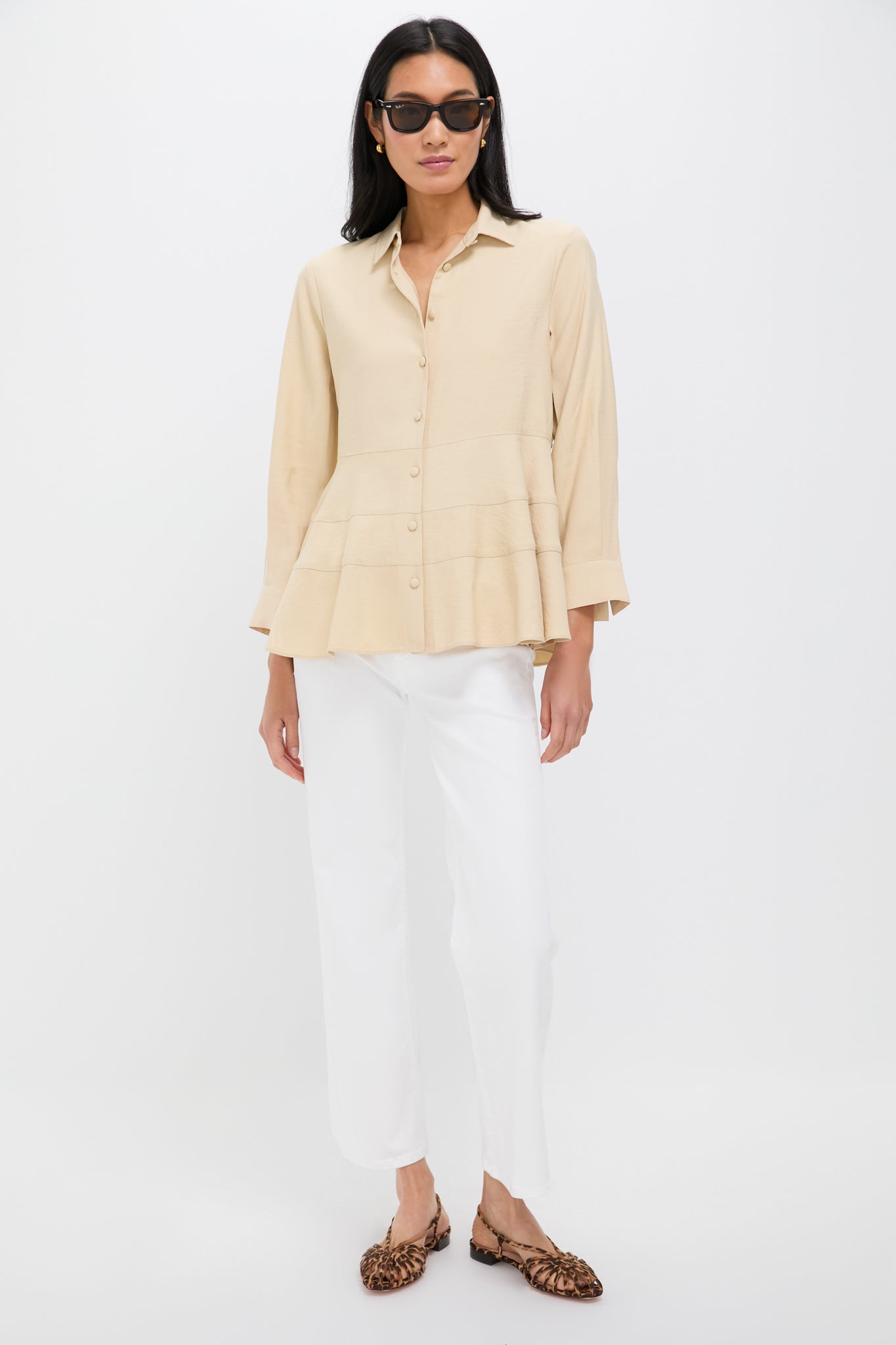 A woman wearing black sunglasses, a Pomander Place Tan Ashlen Blouse with a tiered hem, white pants, and leopard print flats stands confidently.