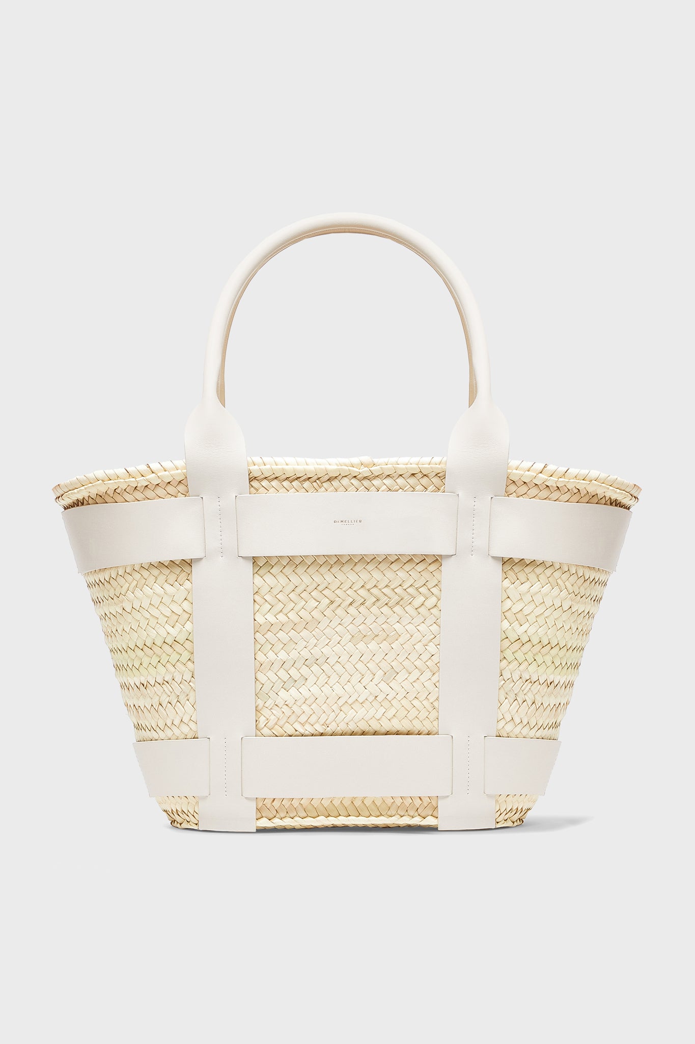 The Demellier Santorini Bag is a woven straw handbag with white leather handles and trim, ideal for those who love handcrafted accessories.