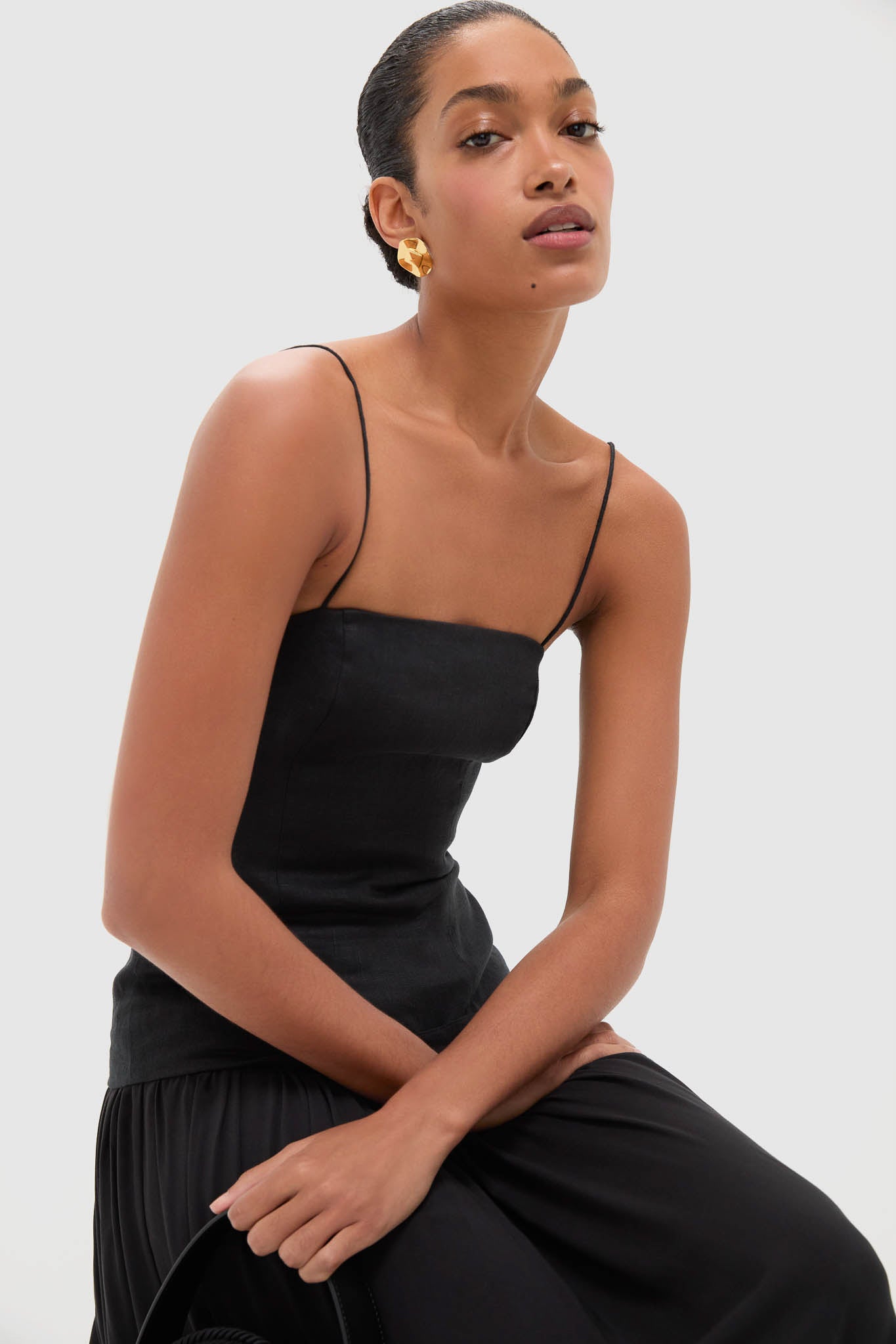 Woman in a classic Black Lenise Maxi Dress with fitted bodice and flowing skirt, accessorized with a chunky gold earring, exuding an effortless, high-end elegance.