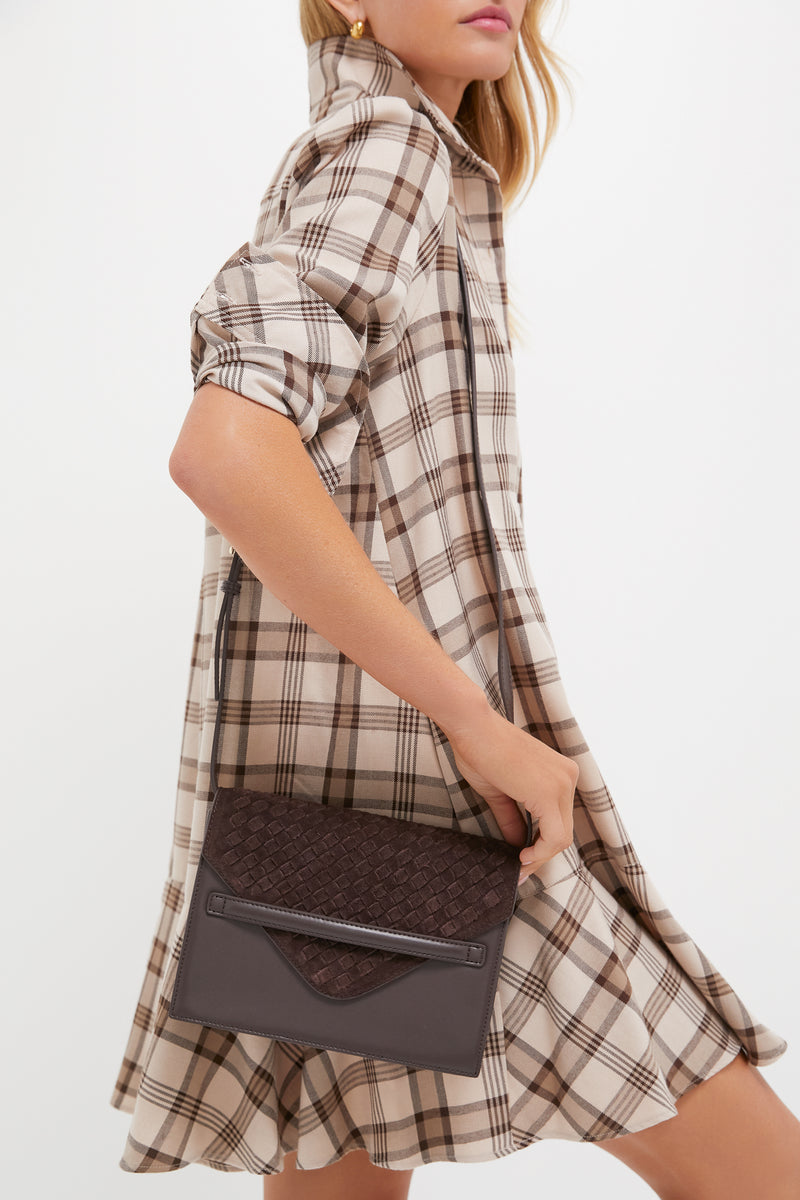 A woman in a beige and brown plaid dress holds a dark brown Tuckernuck Accessories Stevie crossbody at her side, highlighting a chic and hands-free bag option.