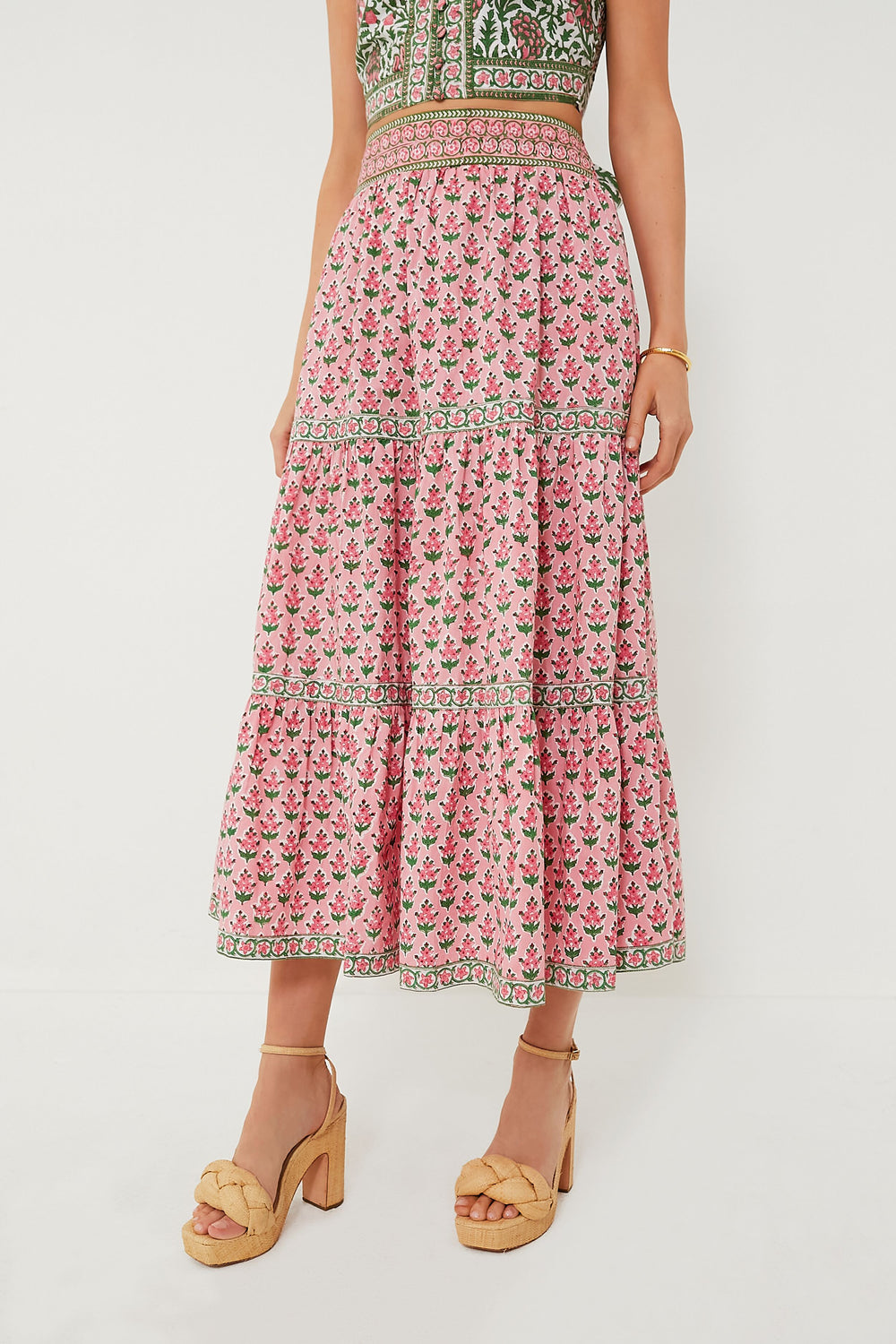 A woman showcases sustainable fashion in Pink City Prints’ pink floral block-printed skirt with a patterned waistband, matching sleeveless top, and beige platform sandals.