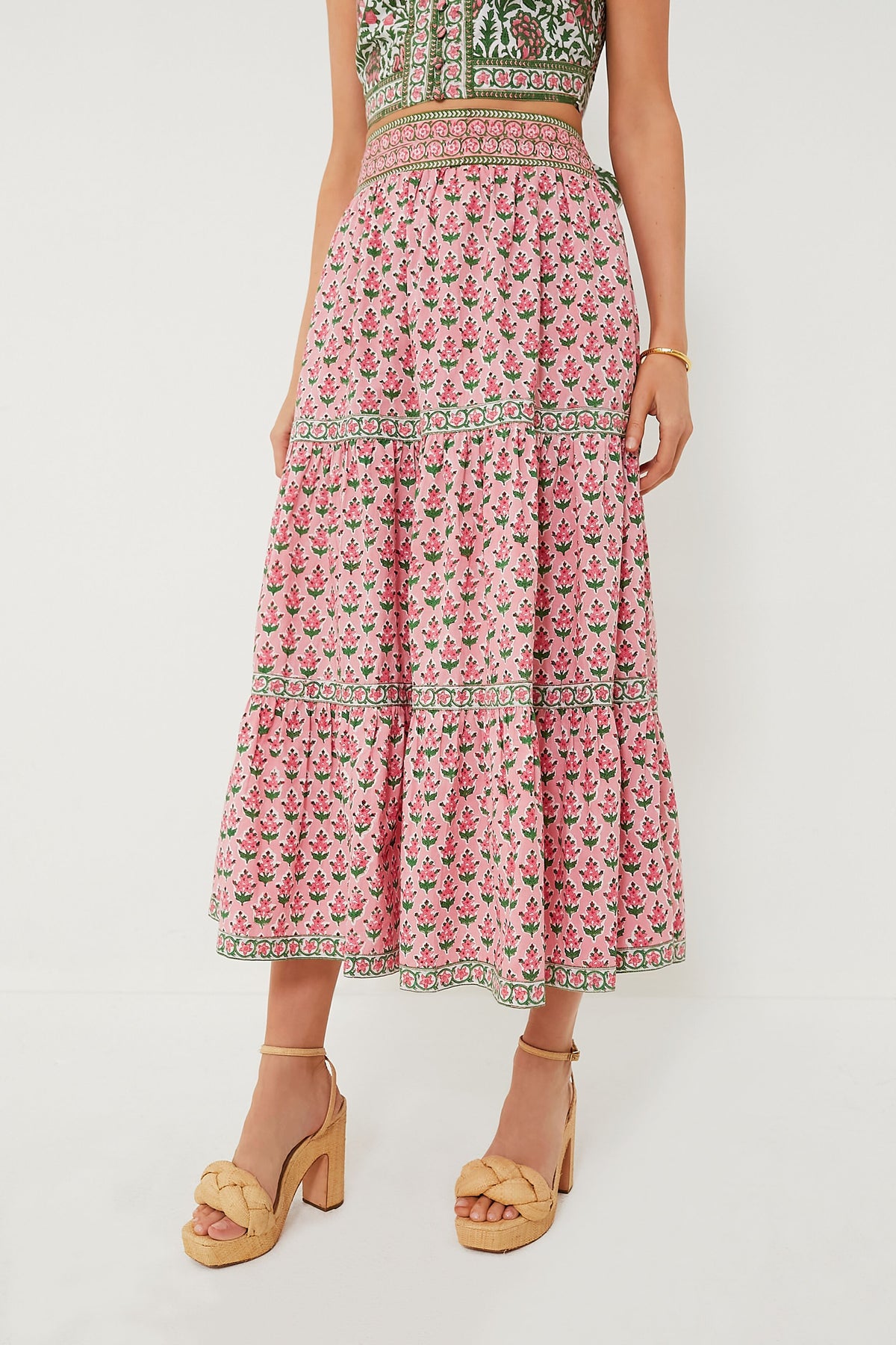 A woman showcases sustainable fashion in Pink City Prints’ pink floral block-printed skirt with a patterned waistband, matching sleeveless top, and beige platform sandals.