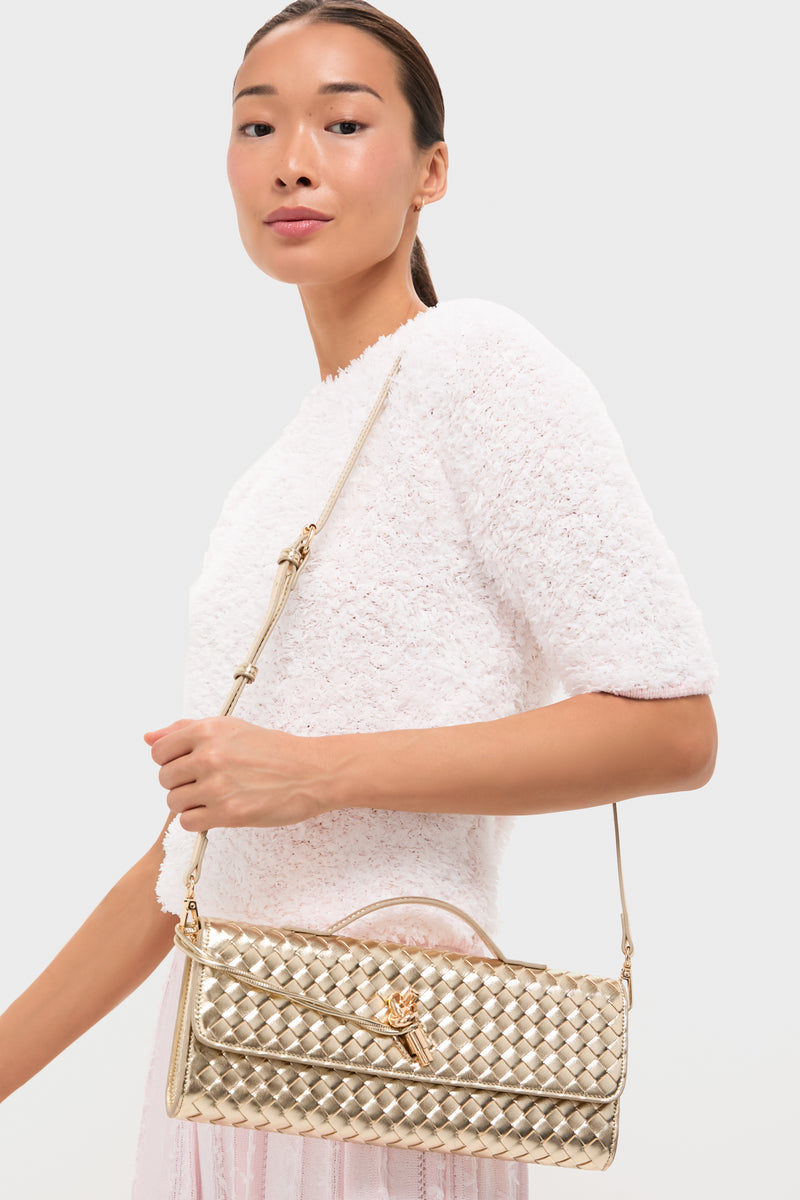 A woman in a textured white top holds the Billini Alice clutch, a gold quilted evening bag with shoulder strap and top handle, against a plain background.