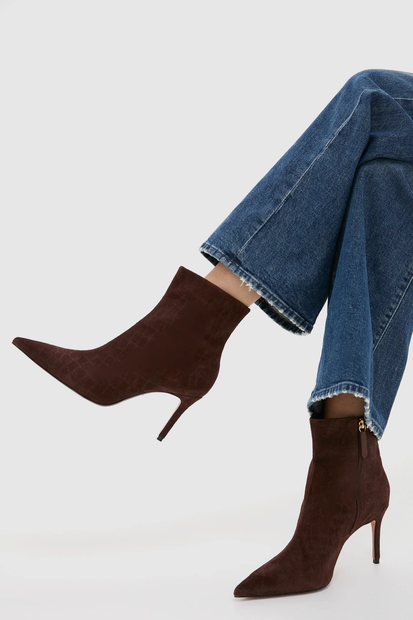 A person wearing cropped blue jeans and brown Schutz pointed-toe heeled ankle boots with side zippers, set against a plain background.