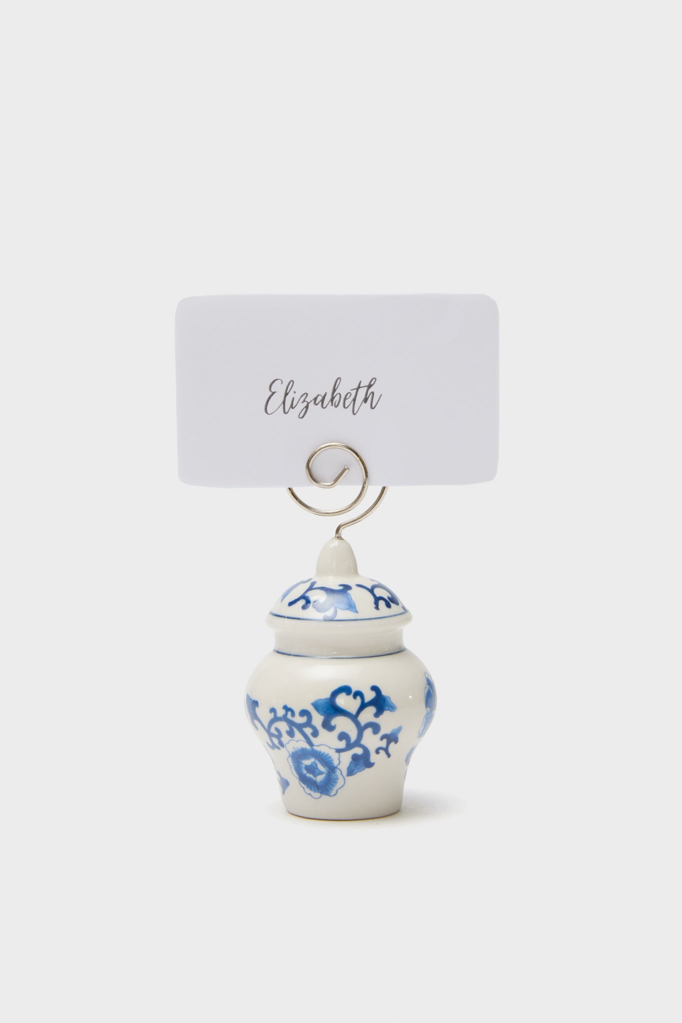 This elegant Ginger Jar Placecard Holder by Two's Company features a small white and blue ceramic jar with a blue floral pattern, metal holder, and a card labeled Elizabeth.