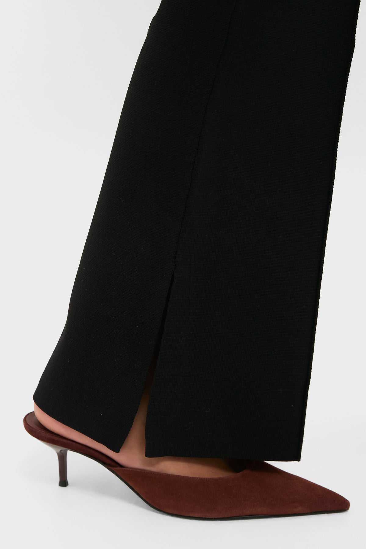 Model wearing Black Hana Pull On Full Flare trousers with a split hem, paired with brown suede kitten-heel slingbacks; a classic, effortless, high-end look.