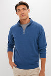 A man wears a blue Peter Millar quarter-zip pullover with a gray t-shirt and beige pants.