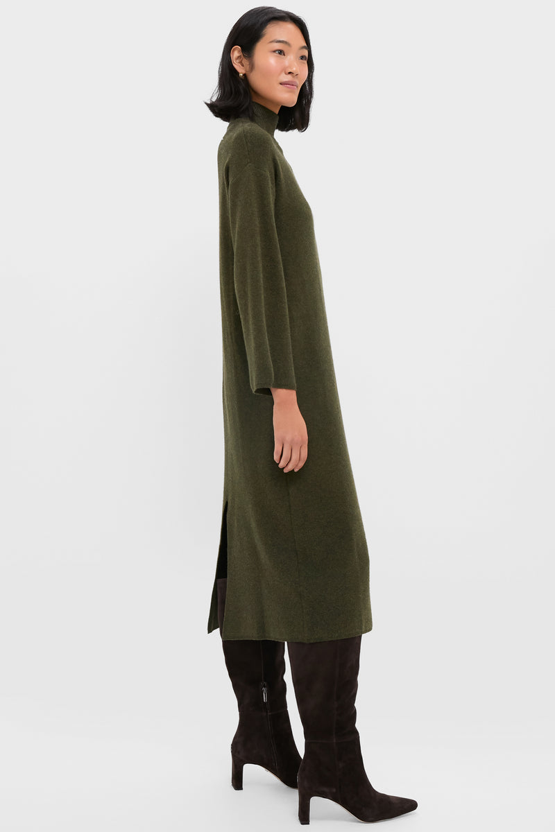 A woman stands in profile wearing the Pomander Place Vivianne Dress, an olive green turtleneck style with a high neck, paired with knee-high dark brown suede boots.