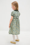 Child in classic Bottle Green Floral Portia Girl Dress with Peter Pan collar, cap sleeves, and fit-and-flare silhouette, embodying effortless, high-end style paired with gold ballet flats.