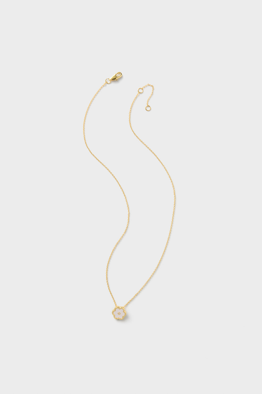 ASHAs Petite Garden Necklace features a delicate 14k gold-dipped chain with a small, flower-shaped pendant and mother-of-pearl center, beautifully displayed against a plain light background.