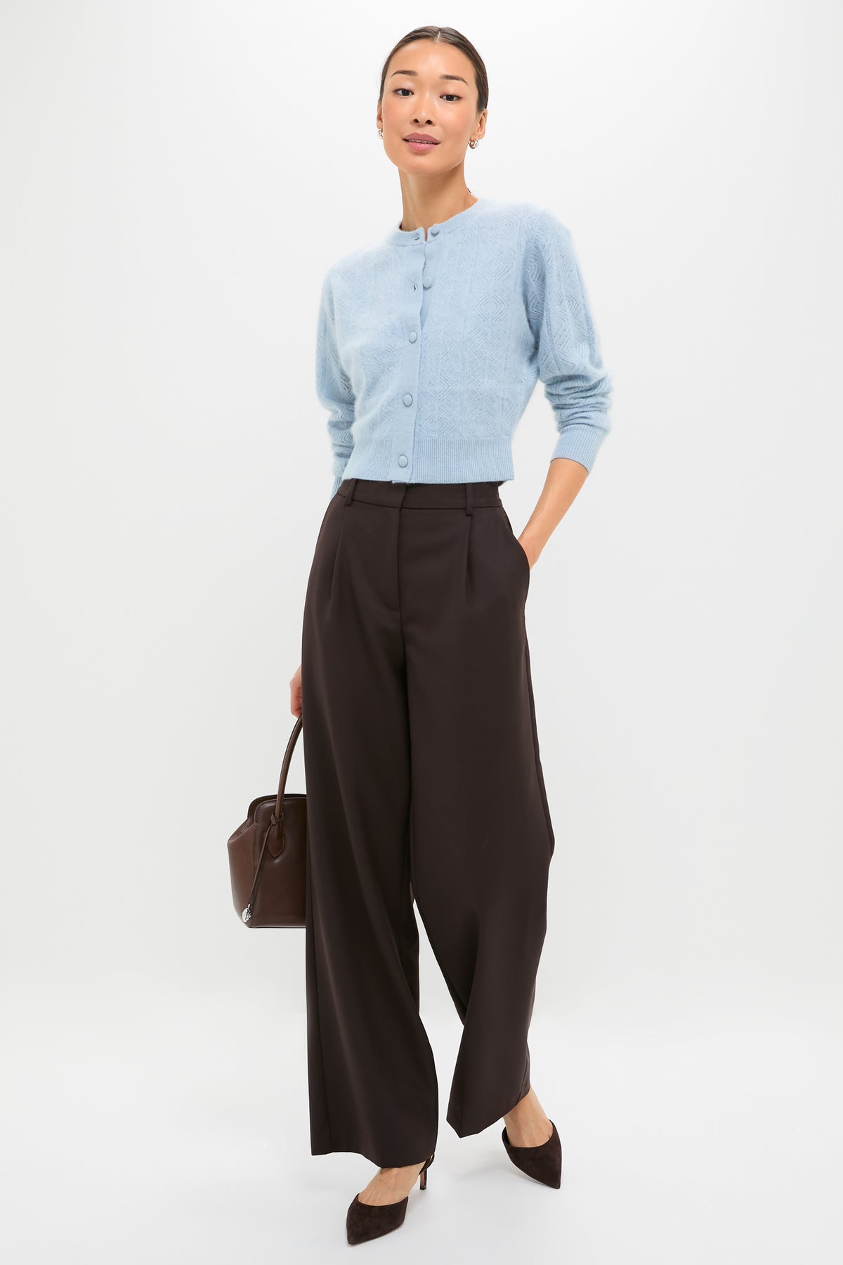 A slim person models the classic Light Blue Brushed Merino Wool Macy Cardigan, paired effortlessly with high-waisted trousers and heels, exuding a fun, high-end style.