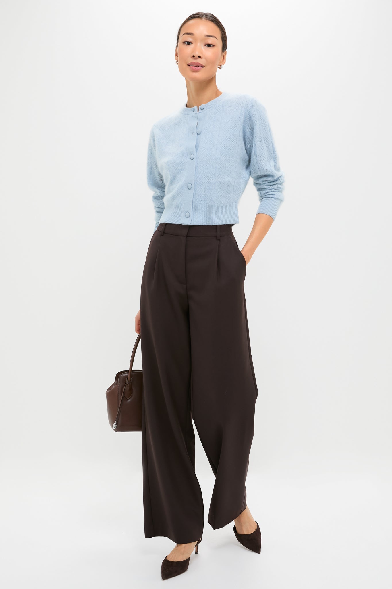 A slim person models the classic Light Blue Brushed Merino Wool Macy Cardigan, paired effortlessly with high-waisted trousers and heels, exuding a fun, high-end style.