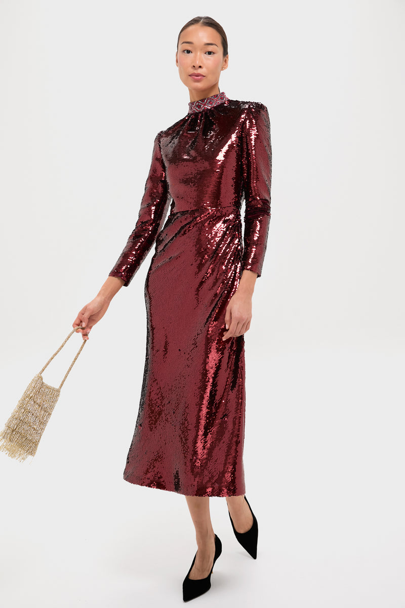 A person wearing a Saloni maroon sequin midi dress with a hand-embroidered neckband holds a beaded tassel purse and pairs it with black pointed-toe heels, standing against a plain white background.