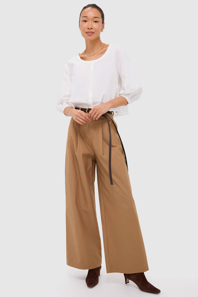 Woman models classic Umber Slubby Cotton Atelier Pleated Pant 2, styled effortlessly with a crisp blouse, black belt, and heeled boots, embodying high-end, fun sophistication.