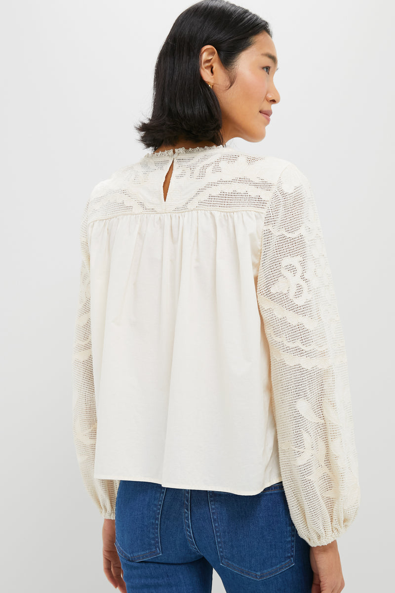 Person modeling the classic Ivory Patchwork Embroidered Cressida Blouse, featuring intricate lace detailing and relaxed puff sleeves, paired effortlessly with mid-blue jeans for a high-end, fun look.