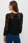Back view of a woman in a classic Black Lace Elodie Blouse with floral lace cutouts, effortlessly paired with jeans and gold hoop earrings for a high-end, fun look.