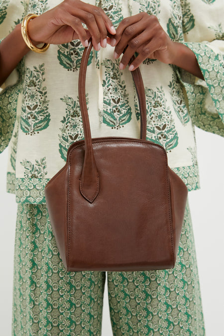 Person holding the Dark Brown Leather Sporty Lady Bag with classic one-handle design, showcasing effortless elegance. The bag features silver-tone hardware and a playful charm.