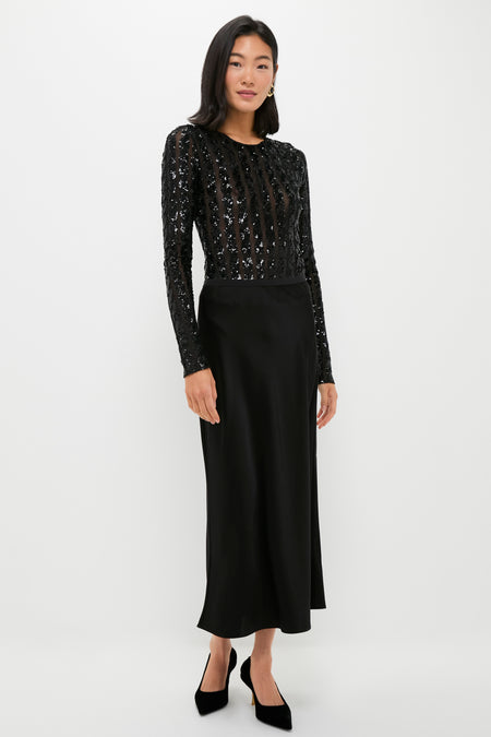 A woman models a Polo Ralph Lauren long black dress with a sequin-embellished bodysuit, sheer long sleeves, and a plain satin skirt—an ideal cocktail party look against a white background.