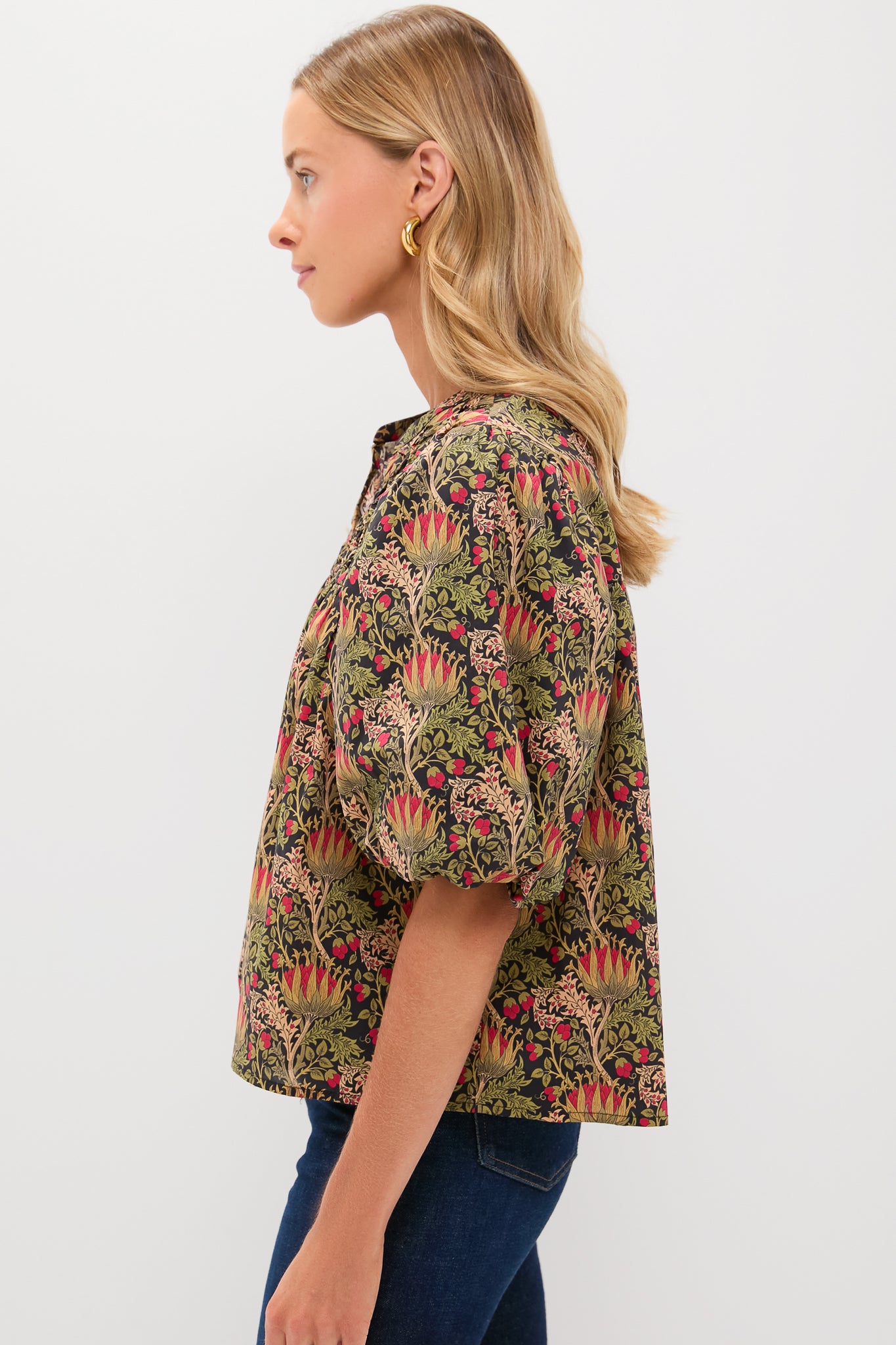 A woman with long blonde hair models a patterned, puff-sleeve blouse and dark jeans from Hyacinth House, standing in profile against a plain white background.