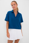 A woman wears a Tnuck Sport blue quick-dry cropped polo with short sleeves and UPF 30 protection, paired with a white pleated skirt.