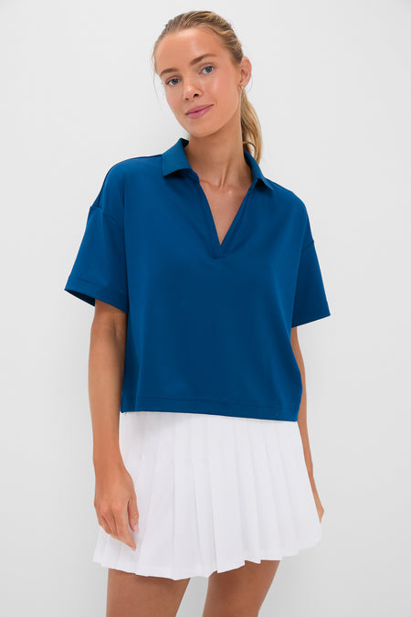 A woman wears a Tnuck Sport blue quick-dry cropped polo with short sleeves and UPF 30 protection, paired with a white pleated skirt.