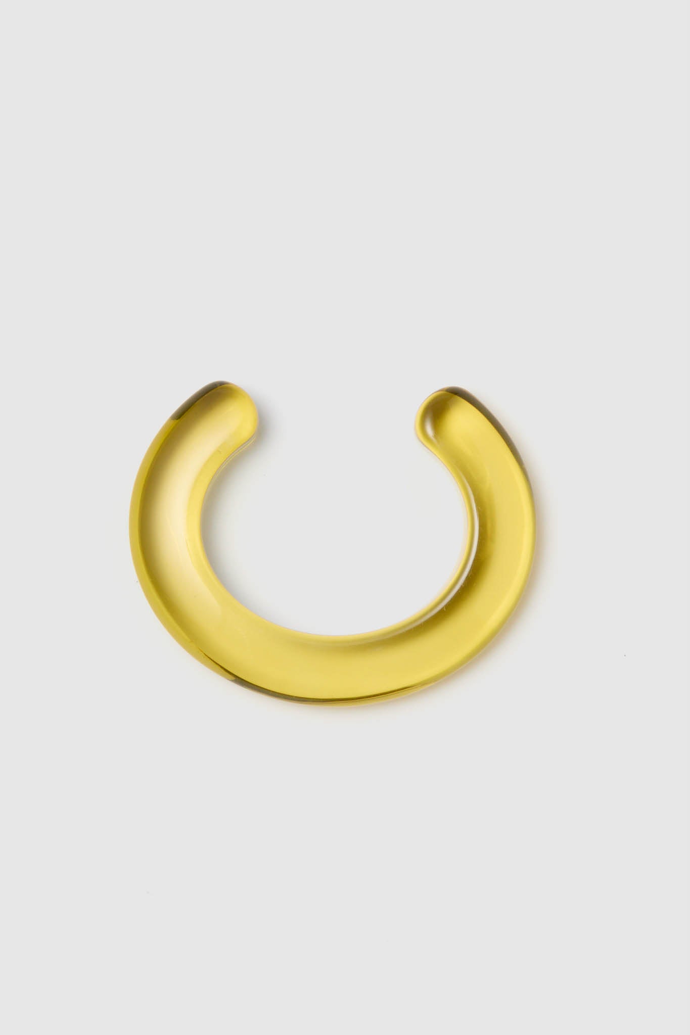 A gold, crescent-shaped metallic object resembling a domed cuff bracelet from Lizzie Fortunato is showcased on a plain light gray surface.