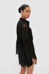 Woman in a Black Lace Long Sleeve Rachael Mini Dress with flared sleeves and scalloped hems, exuding classic, effortless style. Perfect for a chic, high-end look.